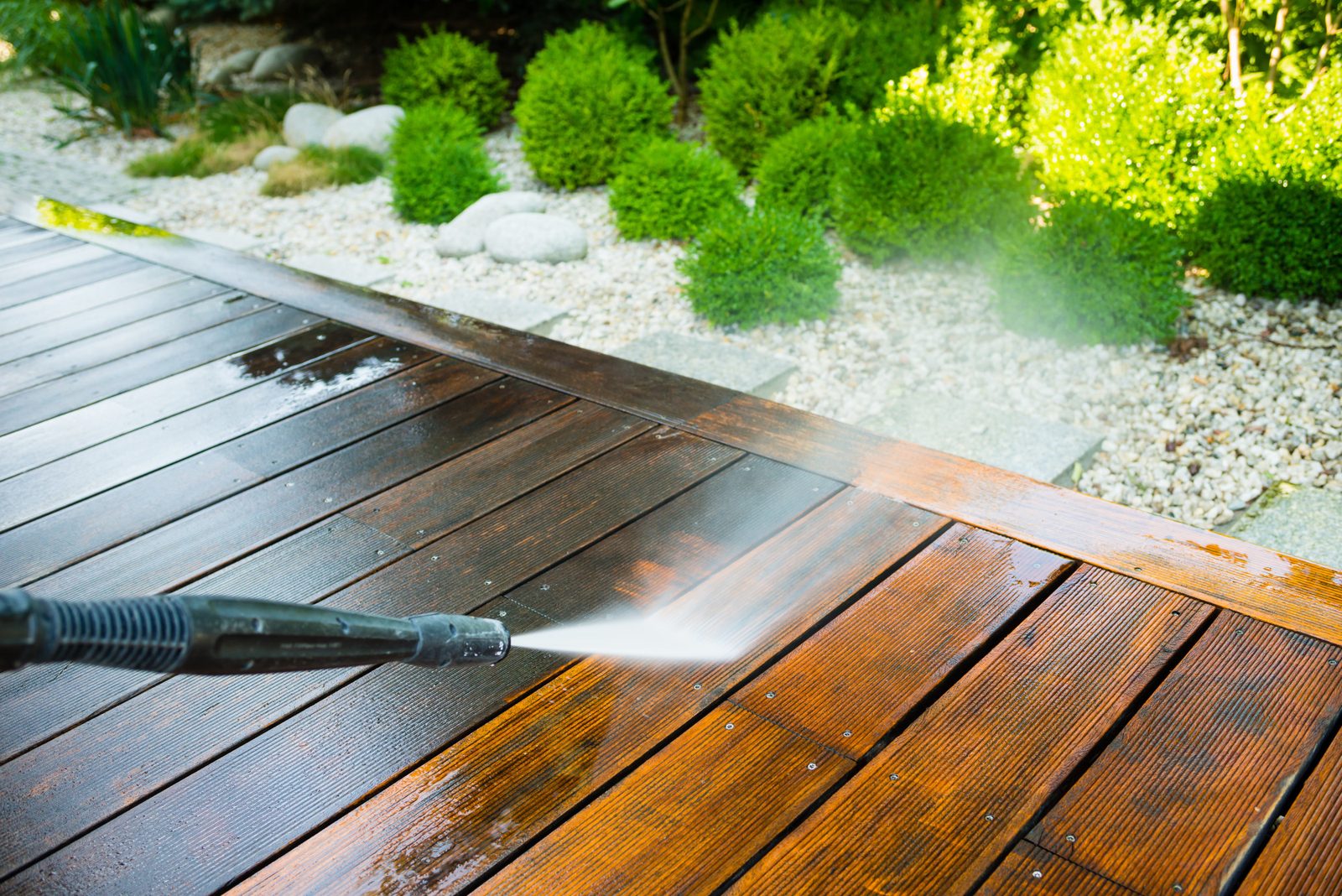 Low pressure wand cleaning a wood deck beside landscaping